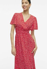 Punane kleit lühikeste lendlevate varrukatega, V-kaelusega ja smockitud vöökohaga. Omab valget abstraktset mustrit üle kogu pikkuse. Kerge kangas.