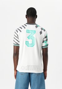 Fehér mez, hátul élénk zöld "3"-as számmal. Csíkos fekete és szürke ujjakkal. "adiTUFF" felirat az alján. Egyszerű, sportos dizájn.