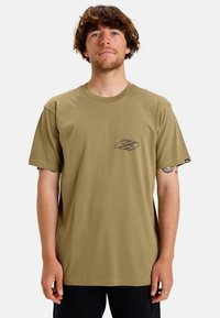 Camiseta de algodón de color verde oliva y manga corta, con un pequeño logo negro en el pecho y un cuello redondo. Diseño sencillo.