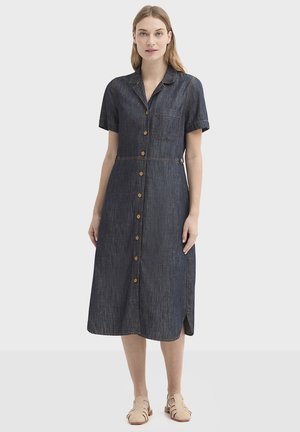 Robe chemise en denim à manches courtes, avec fermeture boutonnée sur le devant, poche poitrine et fentes latérales. Couleur bleu foncé avec couture contrastante.