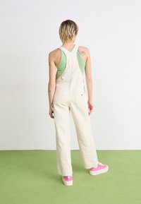 Beige stripete overall med brede ben, laget av bomullsstoff. Kombinert med en grønn topp og rosa platå-sneakers. Bakfra.