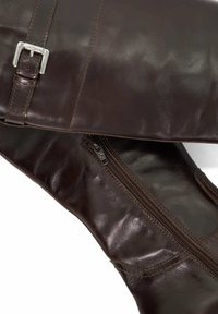 Dark brown leather boots featuring side zipper and adjustable buckle strap with visible stitching details.