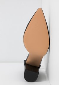 Scarpa con tacco a stiletto nero e punta affusolata. Parte superiore in pelle liscia, suola in gomma testurizzata e soletta di colore nude. Dettagli di cucitura visibili.