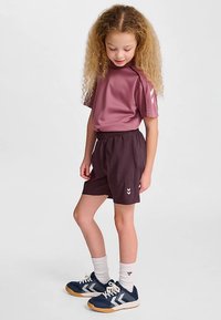 Kort mouwen, mauve sportshirt gecombineerd met donkere korte broek. Voorzien van een elastische tailleband en zijstrepen. Draagt bijpassende marineblauwe sportschoenen en witte sokken.