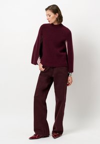 Bordeaux gebreide trui met een hoge kraag en zijslitsen, gecombineerd met bijpassende wijde broek en puntige schoenen. Soepele textuur.