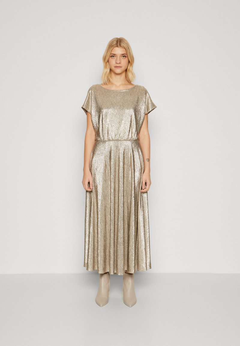 Robe maxi métallique dorée avec des manches courtes, taille élastique, jupe plissée et texture douce, associée à des bottines beiges.