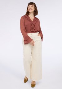 Roestkleurige blouse met ruches van gestructureerde stof, gecombineerd met crèmekleurige hoge taille wijde broek en brown schoenen.