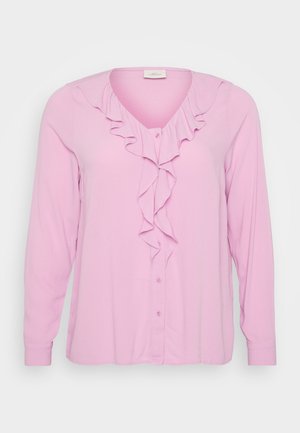 Pink long-sleeve blouse with a V-neck, featuring a front ruffle detail and button closure. Made from a soft, lightweight fabric.