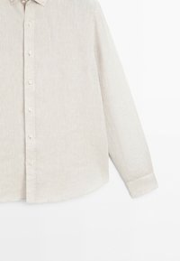 Beige long-sleeve button-up shirt with a collar, shown neatly ironed against a plain white background. Only part of the shirt is visible.