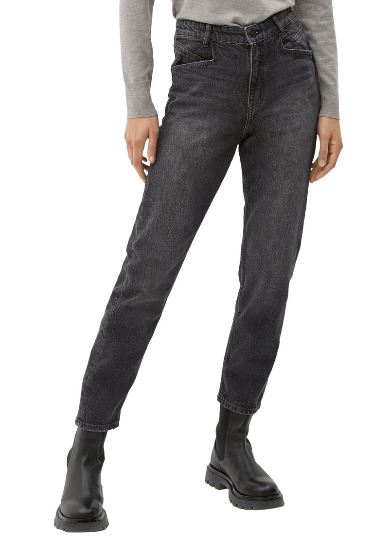 Personne portant un jean noir taille haute délavé et des bottes noires épaisses, debout, jambes légèrement écartées, mains détendues sur les côtés.