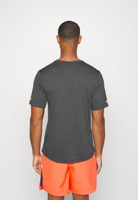 Camiseta corta de manga corta en gris oscuro con un escote redondeado, textura suave y un sutil detalle del logo en la manga. Se lleva con pantalones cortos de color naranja brillante.