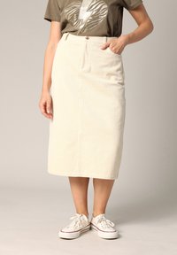 Jupe en velours côtelé crème, longueur genou, avec une texture à côtes verticales, dotée d'une ceinture, d'une poche et associée à des baskets blanches.