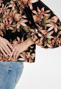 Blusa nera floreale con grandi fiori arancioni e verdi, maniche a campana ampie e vestibilità rilassata, abbinata a jeans denim azzurri chiari.