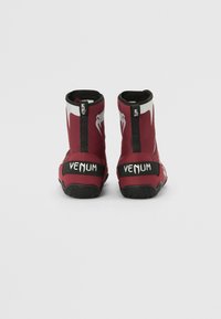 Scarpe da ginnastica rossastre in rete con dettagli neri, caratterizzate da un design a collo alto, un logo Venum e suole in gomma texturizzata per una migliore aderenza.