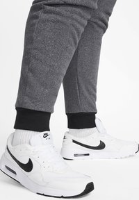 Bílé tenisky Nike Air s černými akcenty, s kombinací síťoviny a kůže na svršku, spárované se šedými tepláky s černými manžetami.