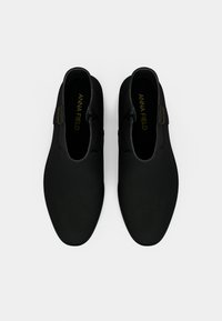 Botas pretas até ao tornozelo com textura lisa, painéis laterais elásticos, bico arredondado e costura mínima. Logotipo discreto da marca por dentro.