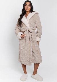 Beige gewatteerde bathrobe met een sjaalkraag, riem en fleece accenten. Heeft een kabelbreipatroon en bijpassende fluffy slippers.