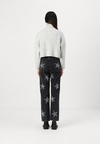 Kuttet grå strikkegenser kombinert med høyt liv svarte denimjeans med sølv stjerne-applikasjoner. Svarte ankelstøvler synlig.
