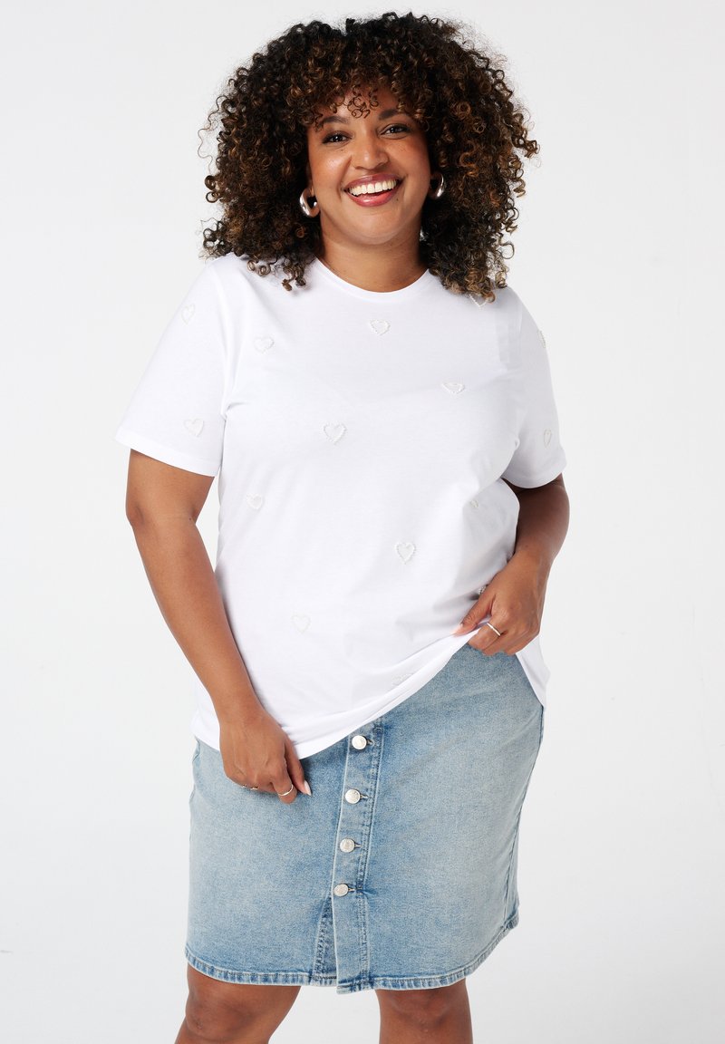 Witte t-shirt met hartvormige reliëfdetails, gecombineerd met een lichtblauwe denimrok met een knoopsluiting aan de voorkant en een rafelende rand.