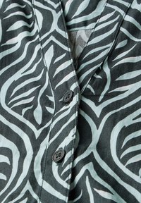 Paita, jossa on mustavihreä zebra-raitakuosi, syvä V-pääntie ja pienet mustat napit. Pehmeä kangas.