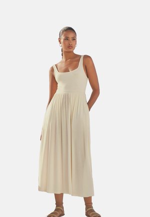 Beiges Maxikleid mit tailliertem Oberteil, breiten Schulterträgern und einem gerafften Rock. Gefertigt aus weichem Stoff mit glatter Textur.