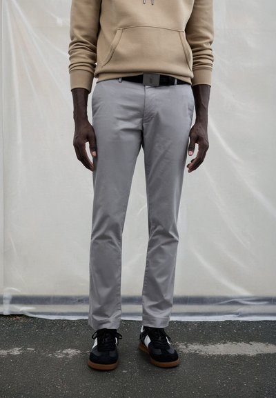 Light gray trousers made of smooth fabric, featuring a slim fit and standard pockets. Worn with black and white sneakers, creating a casual look.