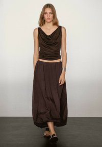 Braunes Top mit Kragen aus seidigem Material, kombiniert mit einem fließenden braunen Rock. Das Outfit zeichnet sich durch einen lockeren Schnitt und dezente Texturdetails aus.