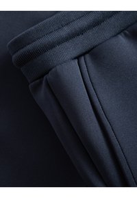 Navy blue athletic fabric featuring a ribbed waistband and smooth, pleated side panel for flexible movement and comfort.