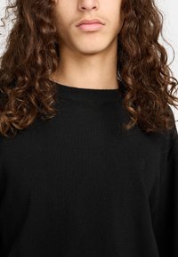 Maglione nero a maglia con scollo rotondo e tessuto struttura. Un piccolo logo tono su tono è posizionato nella zona del petto.