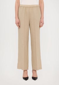 Pantalon large en lin beige avec une taille élastique, présentant une texture lisse et une coupe loose, associé à des escarpins noirs pointus.