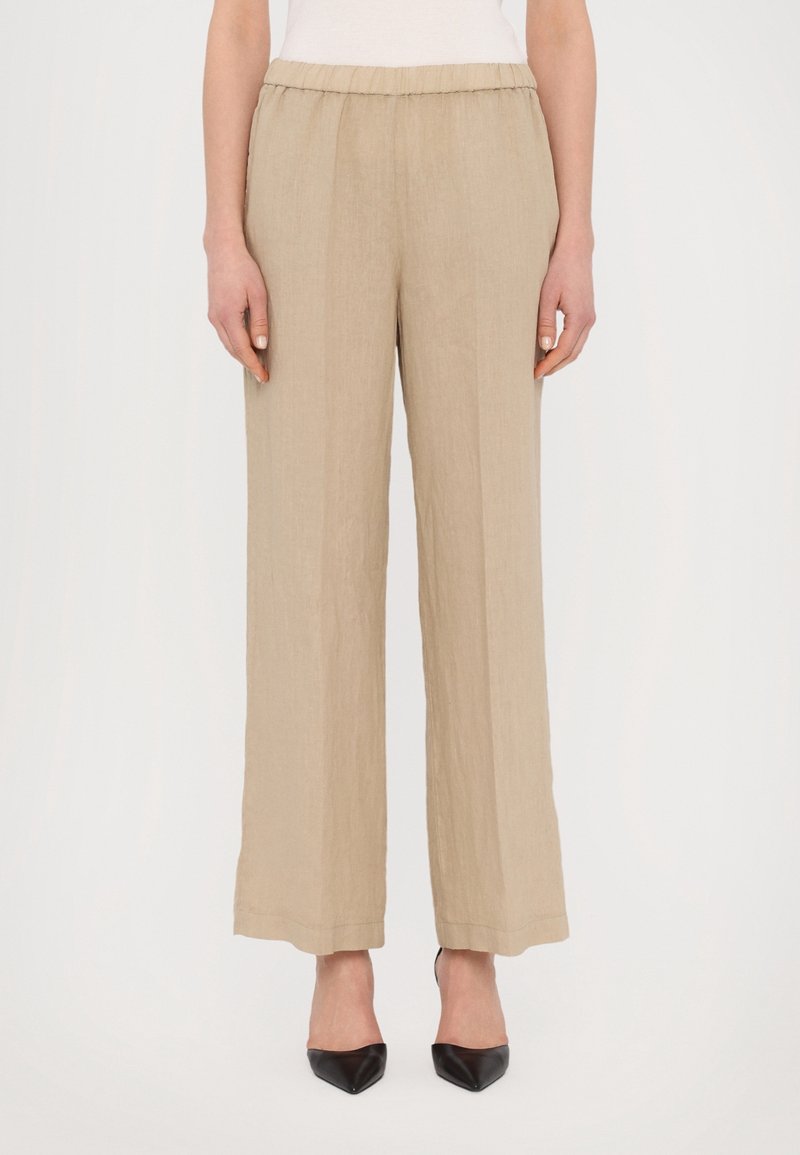 Pantalon large en lin beige avec une taille élastique, présentant une texture lisse et une coupe loose, associé à des escarpins noirs pointus.