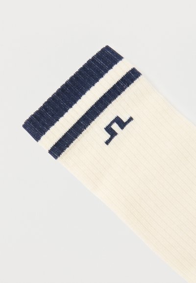 Λευκός κάλτσα με ριγέ σχεδίαση και διπλές ριγέδες σε ναυτικό μπλε χρώμα στην κορυφή, με μικρό λογότυπο σε ναυτικό μπλε χρώμα κάτω από τις ρίγες.