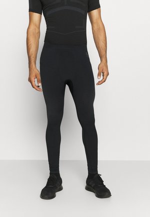 Schwarze Sporttights mit einem strukturierten Muster, figurbetontem Design und elastischem Bund. Getragen mit einem schwarzen T-Shirt mit kurzen Ärmeln und schwarzen Schuhen.