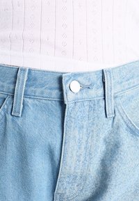 Shorts in denim blu chiaro con vita aderente, chiusura a bottone argentato e una texture sottile con zone sbiadite.