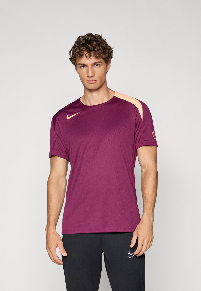 T-shirt atlético bordô com mangas curtas e gola redonda. Apresenta um detalhe contrastante em laranja claro no ombro e o logotipo da Nike.