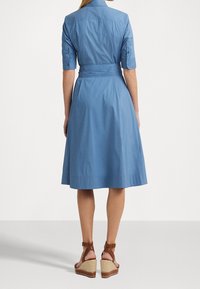 Blaues Baumwollhemdkleid mit tailliertem Schnitt, kurzen Ärmeln und einem ausgestellten Rock. Tragen mit braunen Espadrilles mit Keilabsatz und geflochtenem Absatz.