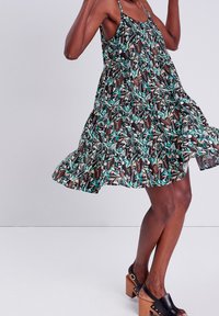 Robe d'été imprimée florale avec des nuances de noir, sarcelle et marron. Elle présente des bretelles fines, une taille froncée et une jupe évasée à volants.