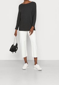 Graues gerippte Langarmshirt, weiße, verkürzte Hose mit fransigen Säumen, weiße Sneaker und eine schwarze Handtasche mit einem silbernen Kettenriemen.