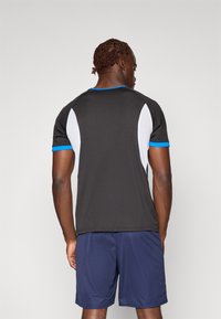 Korte mouwen sportshirt in zwart met blauwe accenten en witte netpanelen. Voorzien van een ronde hals en raglanmouwen. G gedragen met marineblauwe shorts.