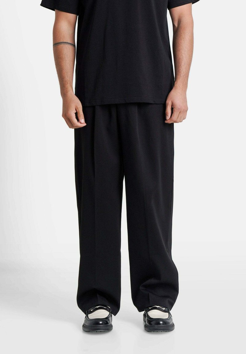 Black loose-fitting trousers with a smooth fabric texture, paired with a matching black oversized t-shirt and black sneakers.