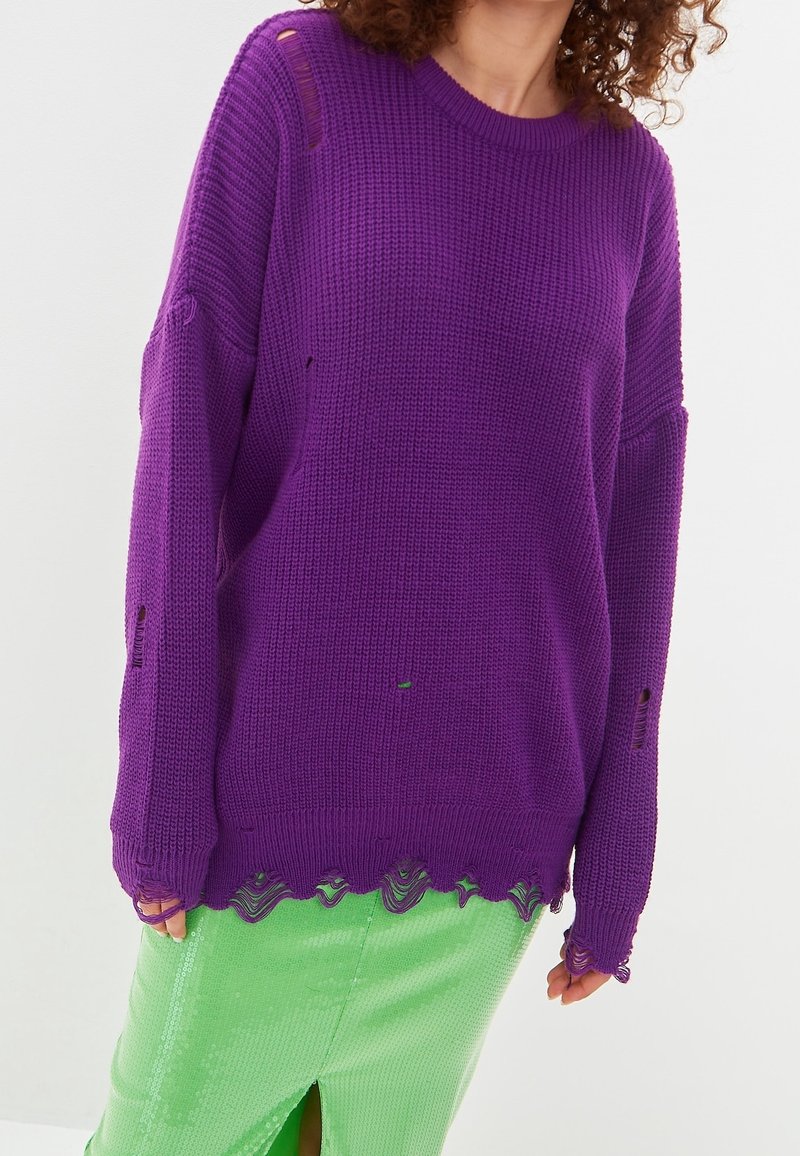 Lila gestrickter Pullover mit lockerer Passform, versehen mit einem abgenutzten Look und einem gewellten Saum. Kombiniert mit einem grünen, Pailletten besetzten Rock.