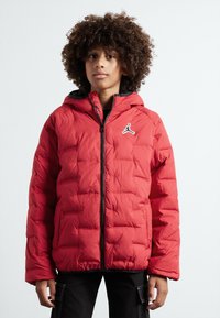 Chaqueta acolchada roja con capucha, cierre de cremallera y detalles en negro, con un logo en el pecho y un diseño acolchado.