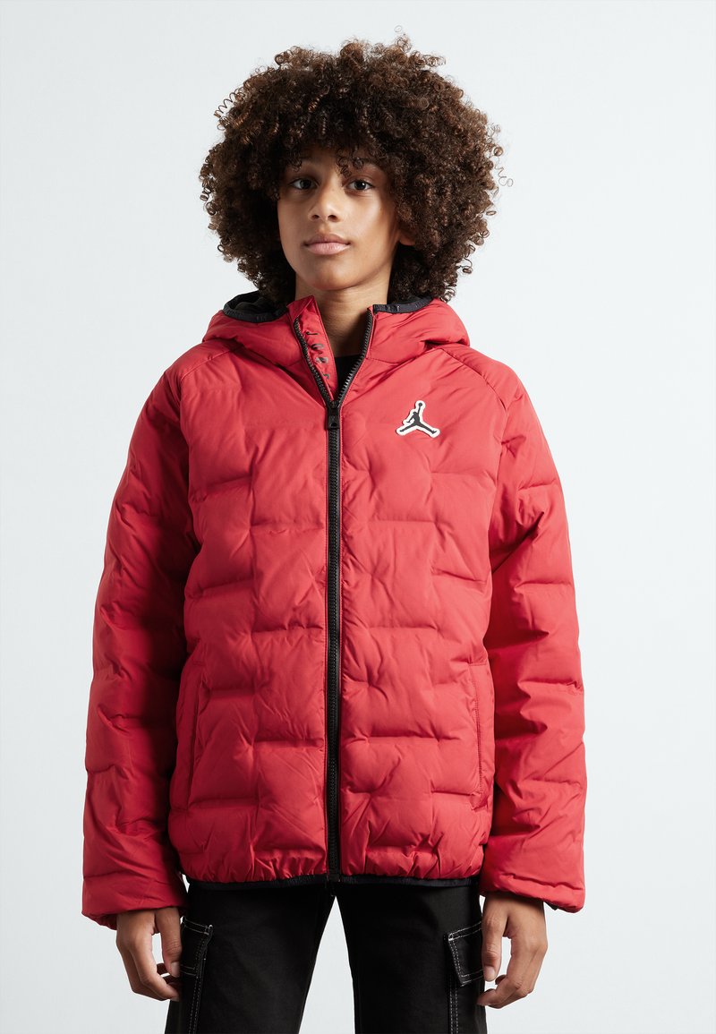 Chaqueta acolchada roja con capucha, cierre de cremallera y detalles en negro, con un logo en el pecho y un diseño acolchado.