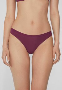 Bas de bikini bordeaux en tissu lisse, avec des bretelles latérales étroites et un design minimaliste. Opaque avec une coupe ajustée.