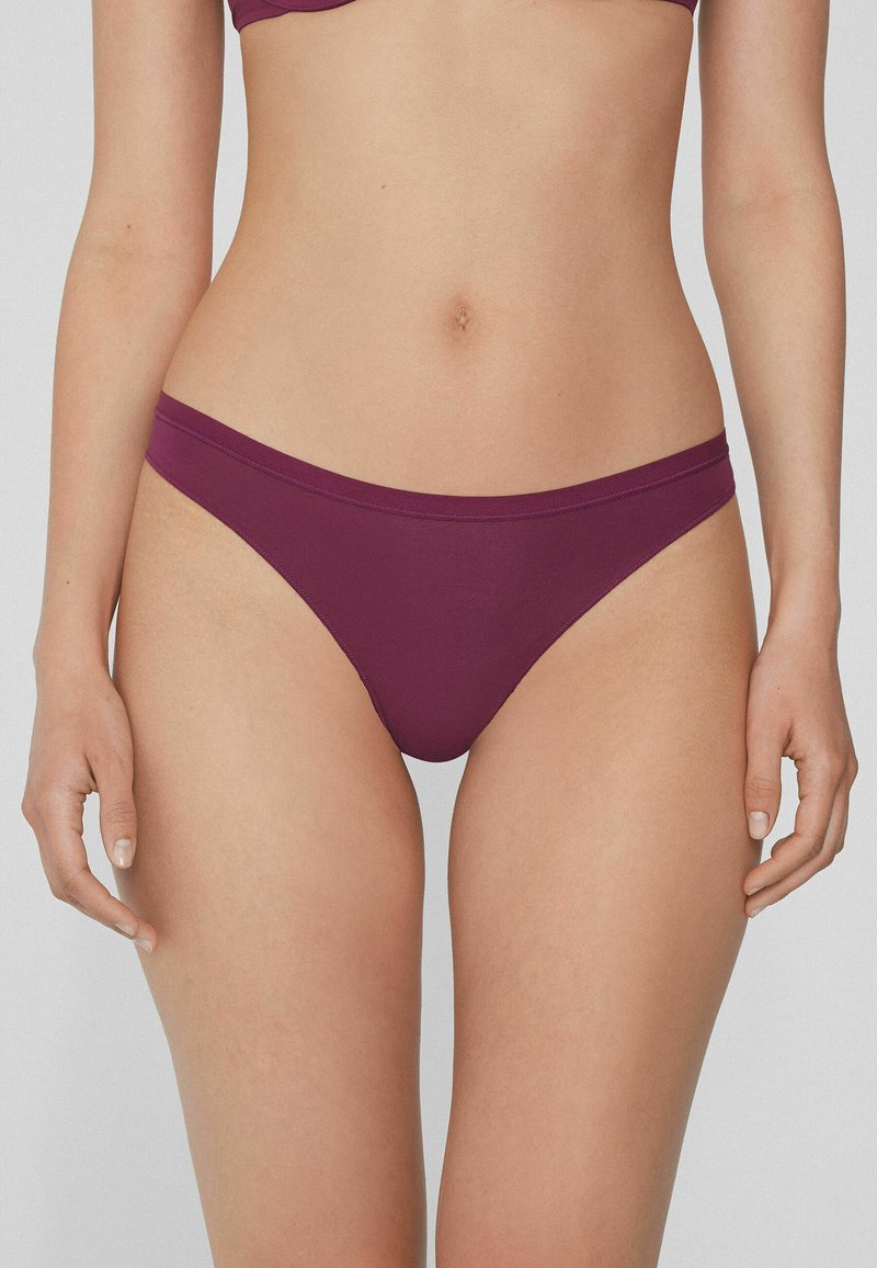 Bas de bikini bordeaux en tissu lisse, avec des bretelles latérales étroites et un design minimaliste. Opaque avec une coupe ajustée.