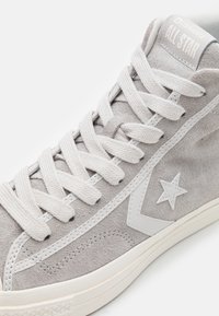 Gray suede high-top sneaker with white rubber sole, textured laces, and a star logo on the side. Features a branded tongue label.