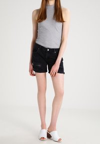 Grijs mouwloos topje gecombineerd met zwarte denimshorts met beschadigde details. Model draagt witte open-toe slippers. Soepele, aansluitende texturen.
