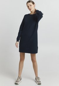 Marinblå sweatshirtklänning med långa ärmar, ribbade manschetter och avslappnad passform. Materialet är slätt med en minimalistisk design.