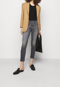 Beżowa marynarka, czarny top, szare dżinsy z wysokim stanem i czarne buty wsuwane. Gładka faktura, dopasowany krój i skrócone nogawki z lekkim przetarciem.