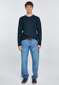 Maglietta henley a maniche lunghe navy con tre bottoni, abbinata a jeans blu chiaro a gamba dritta e sneakers navy con suola in gomma.